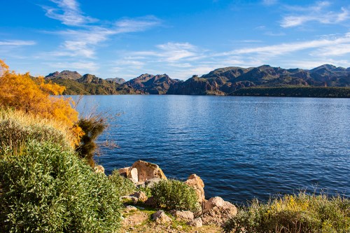 A serene lake surrounded by mountains and greenery under a clear blue sky.