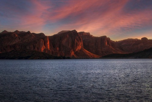 Sunset over a calm lake, with dramatic mountains reflecting warm colors in the sky.