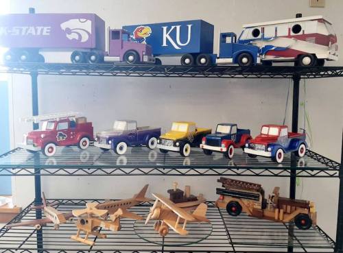 A display of colorful wooden toy vehicles, including trucks, cars, and airplanes, on a metal shelf.
