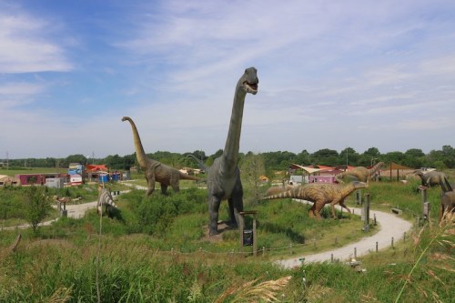 A park featuring large dinosaur sculptures among greenery and pathways under a blue sky.