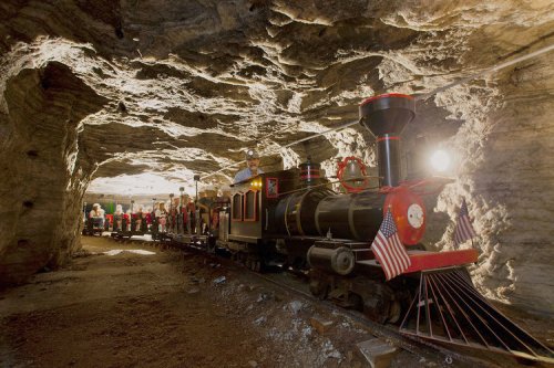 A miniature train inside a cave, with passengers seated, surrounded by rocky walls and dim lighting.