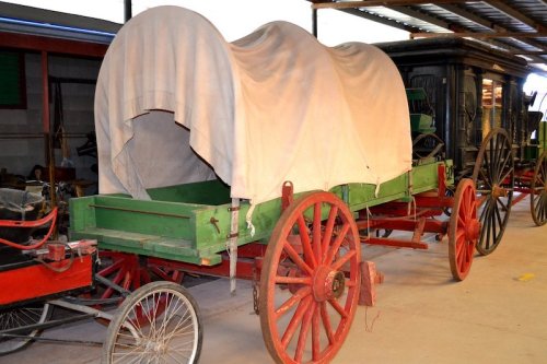 A covered wagon with a white canvas top and green wooden base, displayed in a museum setting.