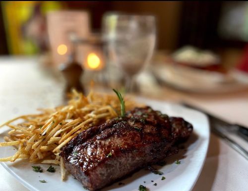 A plate of grilled steak garnished with herbs, served with a side of crispy fries on a table setting.