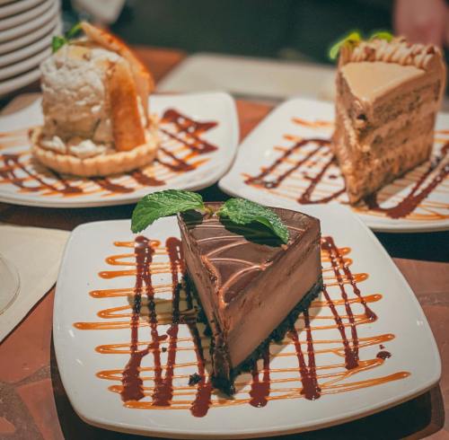 Three dessert plates featuring chocolate cake, cheesecake, and a slice of caramel cake, drizzled with chocolate sauce.