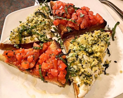 Four slices of toasted bread topped with diced tomatoes, herbs, and a green mixture on a white plate.