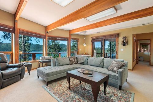 Cozy living room with large windows, a sectional sofa, and a coffee table, overlooking a scenic lake view.