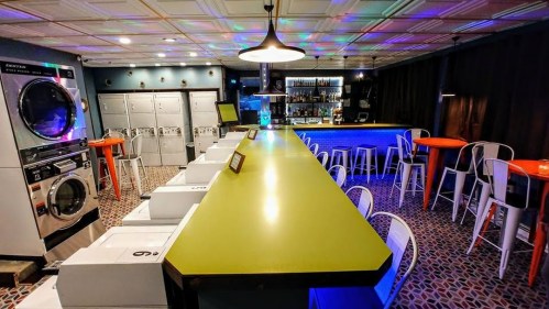 A modern laundromat bar featuring a bright green counter, colorful stools, and washing machines in a stylish setting.