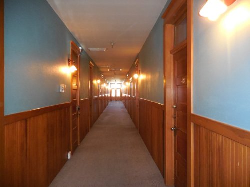 A long, well-lit hotel hallway with wooden doors and blue walls, featuring warm lighting along the sides.