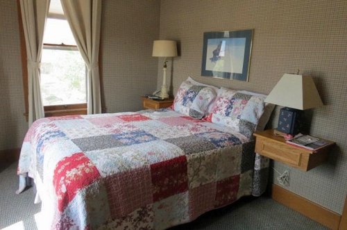 Cozy bedroom featuring a quilted bedspread, bedside tables, and a window with natural light.
