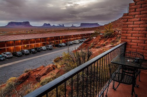 View from a balcony overlooking a desert landscape with rock formations and a parking lot below under a cloudy sky.