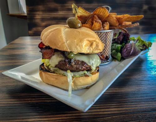 A juicy burger with cheese, lettuce, and toppings, served with a side of crispy potato chips on a white plate.