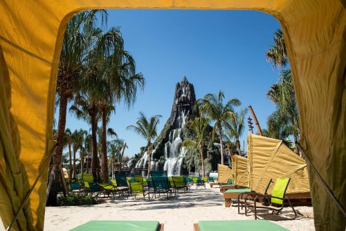 View from a cabana showing a tropical pool area with palm trees and a large waterfall feature in the background.
