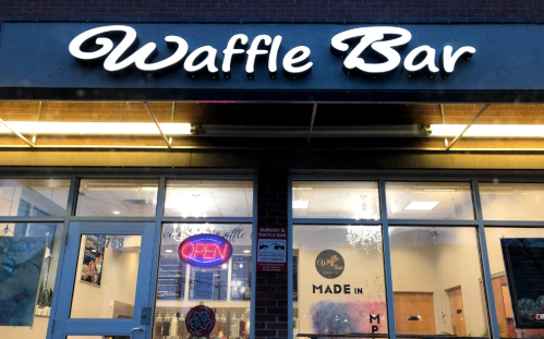 Exterior of Waffle Bar with illuminated sign, "OPEN" neon light, and welcoming storefront.
