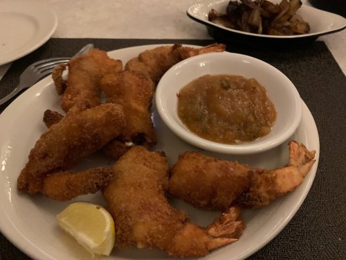 A plate of fried shrimp with a lemon wedge and dipping sauce, served alongside a side of cooked vegetables.