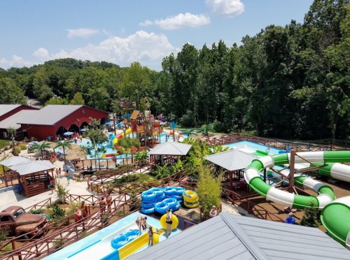 Aerial view of a water park featuring slides, pools, and lush greenery in the background.