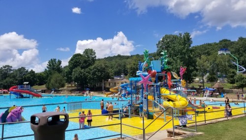 A vibrant water park with slides, a splash area, and families enjoying the sunny day by the pool.