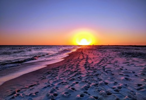 A serene beach at sunset, with footprints in the sand and vibrant colors in the sky reflecting on the water.