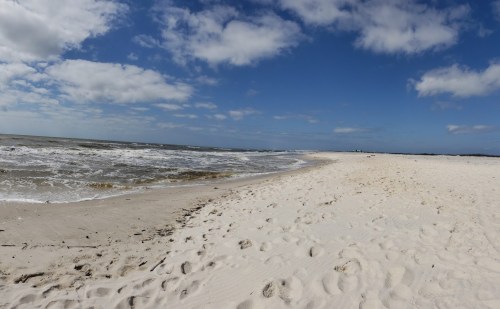 A sandy beach with gentle waves, under a blue sky filled with fluffy clouds.