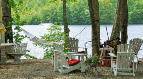 A serene lakeside scene with chairs, a hammock, and greenery, inviting relaxation by the water.