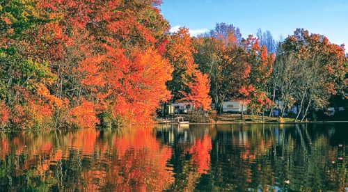 A serene lake surrounded by vibrant autumn foliage reflecting on the water, with a cozy cabin in the background.