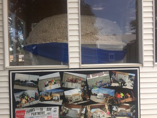 A large mound of popcorn displayed in a window, with a sign featuring photos of community partners and events below.