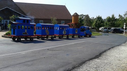A colorful children's train ride parked on a paved path near a building and trees on a sunny day.
