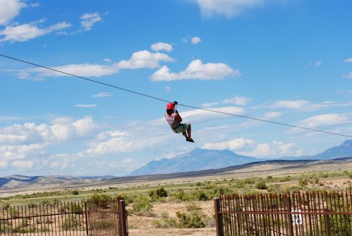 A person zip-lining across a vast landscape with mountains and blue skies in the background.