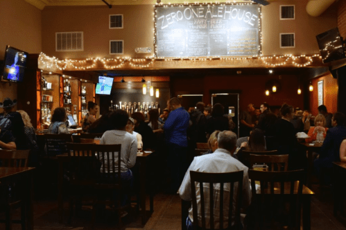 A lively bar scene with patrons enjoying drinks and food, warm lighting, and a chalkboard menu in the background.