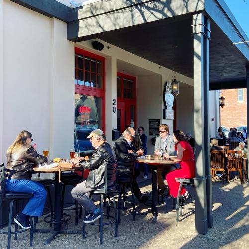 A group of people dining outside a restaurant, enjoying food and drinks under a sunny sky.