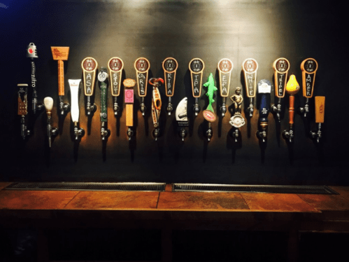 A wall-mounted beer tap system with various taps and handles, showcasing a variety of beer options.