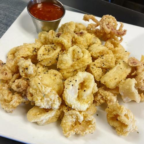 A plate of crispy fried calamari served with a small cup of marinara sauce.