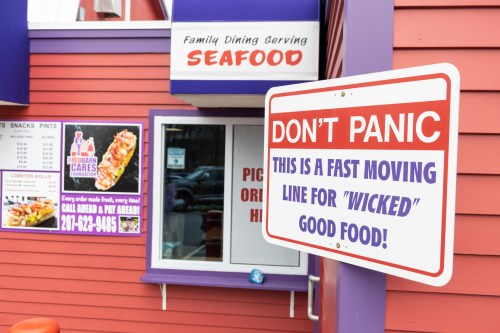 Sign outside a seafood restaurant reads, "Don't Panic! This is a fast moving line for 'Wicked' good food!"