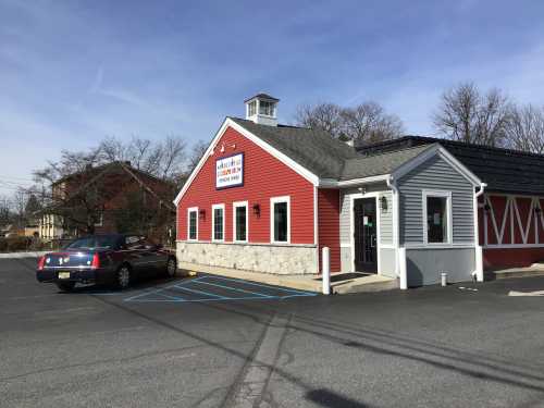 A red and gray building with a stone foundation, featuring a sign and a parked car in front.