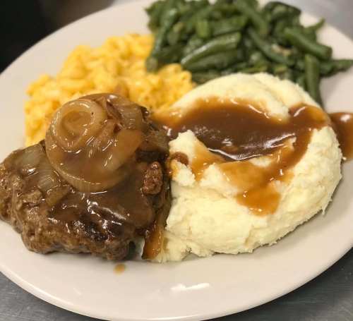 A plate featuring meatloaf with onions, mashed potatoes with gravy, macaroni and cheese, and green beans.