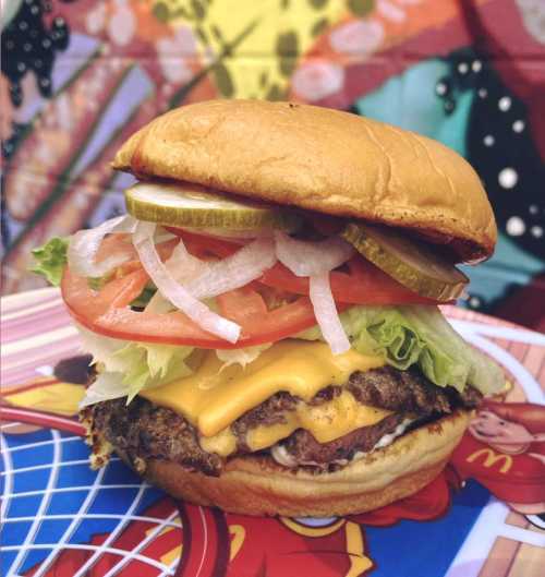 A close-up of a juicy cheeseburger with lettuce, tomato, pickles, and onions on a colorful background.