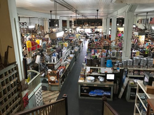 A wide view of a vintage general store filled with various goods, shelves, and displays in a bustling atmosphere.