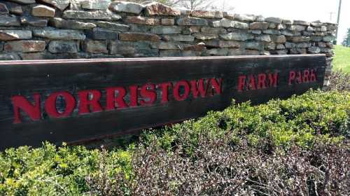 Sign for Norristown Farm Park, featuring stone wall and greenery in the foreground.