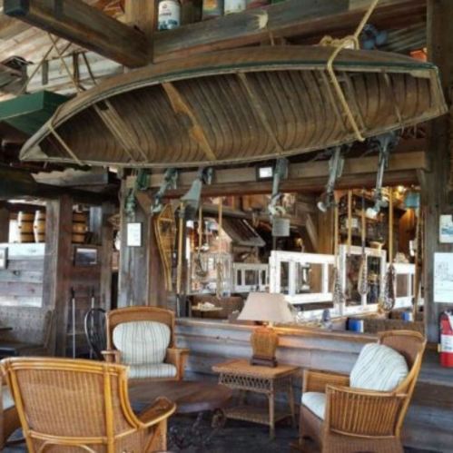 A rustic interior featuring a hanging boat, wicker chairs, and wooden decor in a cozy, nautical-themed space.