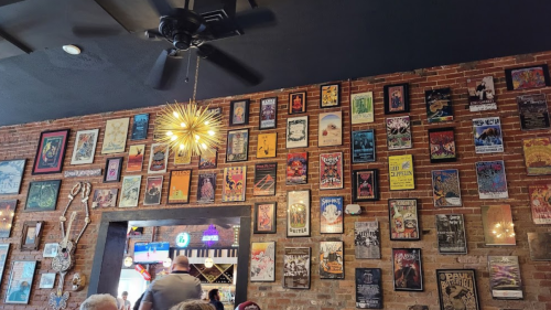 A brick wall adorned with various framed posters and artwork, with a ceiling fan and a modern light fixture.
