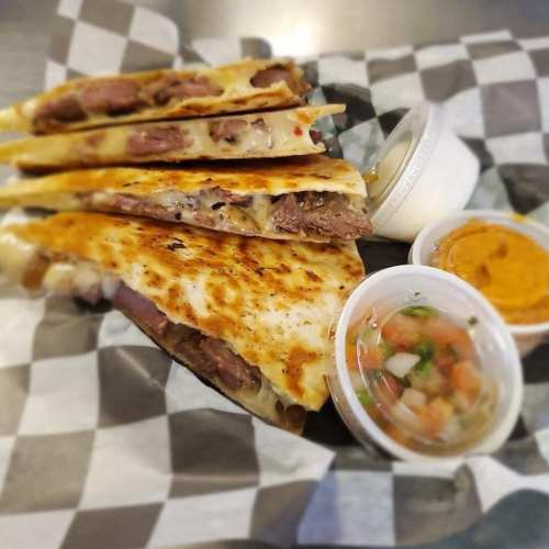 A plate of quesadillas filled with meat and cheese, served with salsa and dipping sauce in small containers.