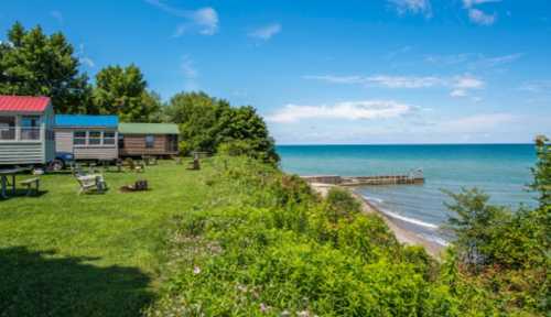 Cozy cabins by the shore, lush green grass, and a serene lake under a clear blue sky.