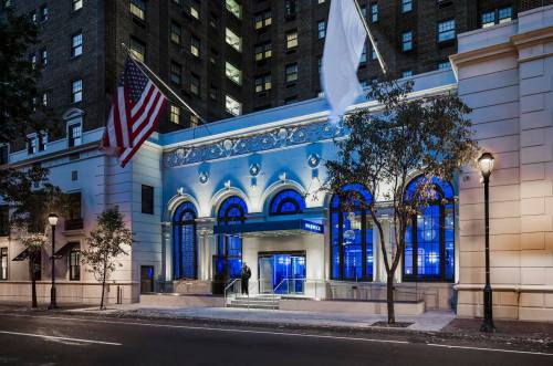 Exterior view of a building with blue lighting, featuring large arched windows and flags, set on a city street.