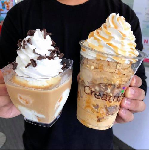 A person holding two dessert cups: one with whipped cream and chocolate shavings, the other with caramel and nuts.