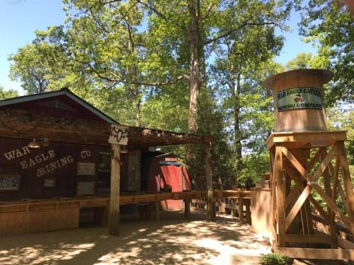 A rustic mining company building surrounded by trees, featuring a wooden water tower and outdoor display area.