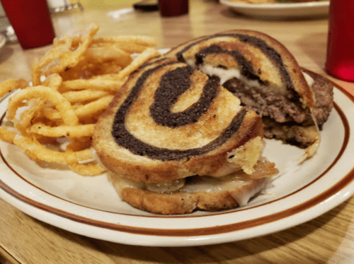 A plate with a sliced sandwich made of swirl bread, filled with meat and cheese, alongside curly fries.