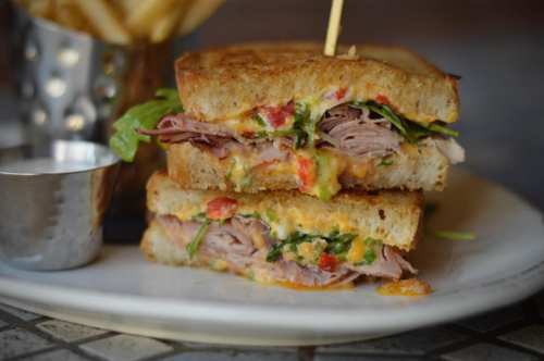 A stacked sandwich with layers of meat, cheese, and greens, served with a side of fries and dipping sauce.