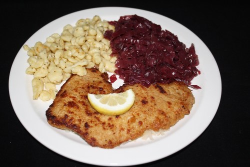 A plate featuring breaded fish with a lemon slice, served with red cabbage and pasta.