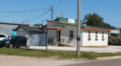 A small, one-story building with a green roof and a sign for "Clyde's Place" offering rate lunches.