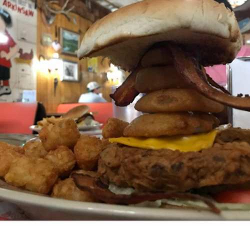 A towering burger with bacon, cheese, and onion rings, served with tater tots in a cozy diner setting.