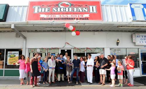 A group of people gathers outside "The Sicilian II" restaurant for a ribbon-cutting ceremony, celebrating its opening.